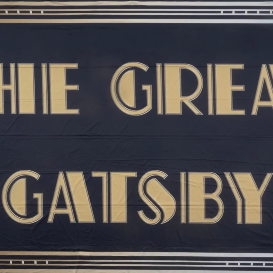 Horyzont Gatsby Napis. Tło fotograficzne w stylu "Wielkiego Gatsby'ego", z eleganckim złoto-czarnym wzornictwem i wyrazistym napisem "THE GREAT GATSBY" w centralnym punkcie. Stylizacja art deco i luksusowa kolorystyka idealnie nadają się na ekskluzywne przyjęcia i eventy tematyczne, wprowadzając atmosferę przepychu i dekadencji charakterystyczną dla ery jazzu - rent4events.pl wypożycz wrażenia, rent4wedding.pl zachowaj wspomnienia.