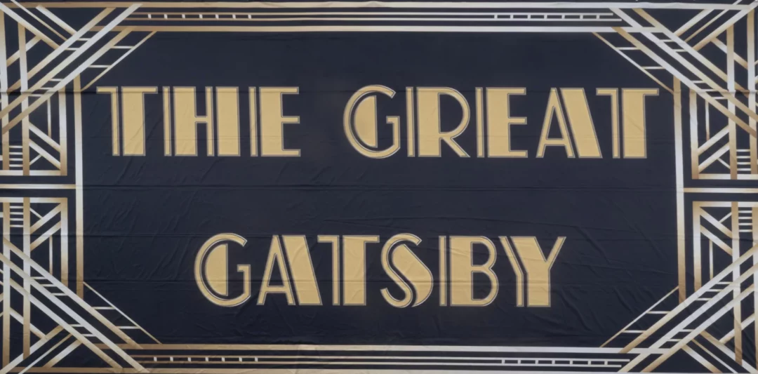 Horyzont Gatsby Napis. Tło fotograficzne w stylu "Wielkiego Gatsby'ego", z eleganckim złoto-czarnym wzornictwem i wyrazistym napisem "THE GREAT GATSBY" w centralnym punkcie. Stylizacja art deco i luksusowa kolorystyka idealnie nadają się na ekskluzywne przyjęcia i eventy tematyczne, wprowadzając atmosferę przepychu i dekadencji charakterystyczną dla ery jazzu - rent4events.pl wypożycz wrażenia, rent4wedding.pl zachowaj wspomnienia.