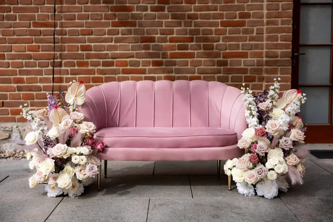 Elegancka różowa sofa welurowa otoczona romantycznymi bukietami kwiatowymi w pastelowych odcieniach, idealnie komponuje się z ciepłą cegłą na tle. Perfekcyjny wybór na ślub czy wesele od wypożyczalni dekoracji RENT4EVENTS. Znakomita scenografia i wysokiej jakości asortyment z Wrocławia, dostępne na rent4events.pl oraz rent4weddings.pl. Wypożycz wrażenia, zachowaj wspomnienia. Fot. BUCHOLCe @bucholce.