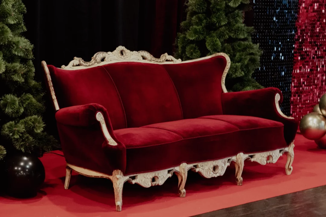 Sofa Barokowa Królewska w świątecznej aranżacji. Czerwona, welurowa sofa w stylu vintage z zdobionymi elementami rzeźbioniej ramy stanowi centralny punkt świątecznej aranżacji. Sofa otoczona jest zielonymi choinkami oraz świątecznymi dekoracjami, co tworzy przytulną i elegancką atmosferę. Te wyjątkowe dekoracje dodają uroku każdej uroczystości, zapewniając niezapomnianą oprawę - rent4events.pl wypożycz wrażenia, rent4weddings.pl zachowaj wspomnienia. Fot. @karolinakiec_fotografia.