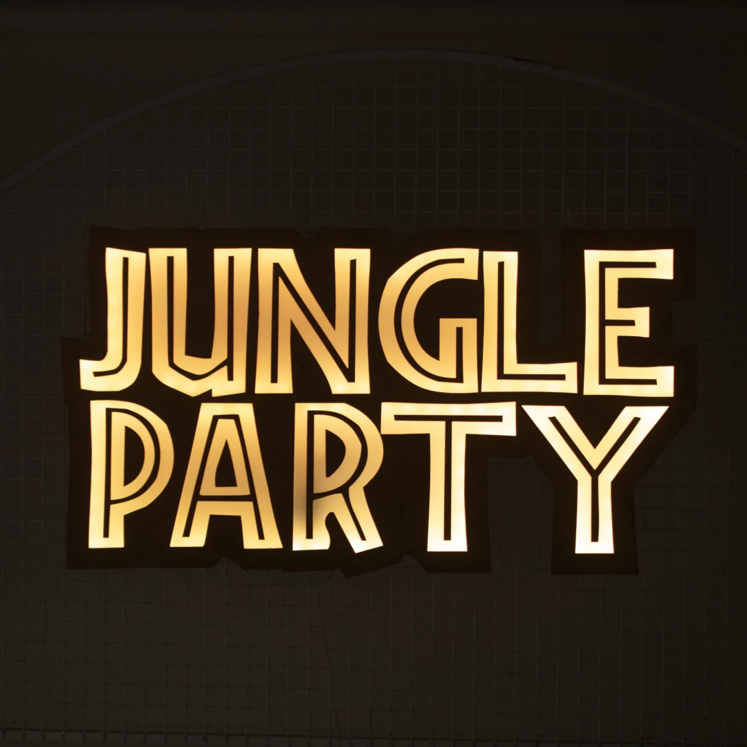 Neonowy napis "Jungle Party" w jasnym żółtym kolorze, napis w drewnochodnej sklejce, idealnie wpisujący się w dekoracje na eventy tematyczne, takie jak w stylu jungle. Dziki estetycznemu wyglądowi na drewnianej sklejce neon wyglada dobrze nawet jak nie jest całkiem ciemno, a zapalony wyróżnia się i przyciąga uwagę, idealnie nadając się do wykorzystania na imprezach i eventach organizowanych we Wrocławiu. Ten element scenografii można wynająć w wypożyczalni dekoracji na rent4events.pl oraz rent4weddings.pl, które oferują szeroki wybór dekoracji na różne okazje - rent4events.pl wypożycz wrażenia, rent4wedding.pl zachowaj wspomnienia.