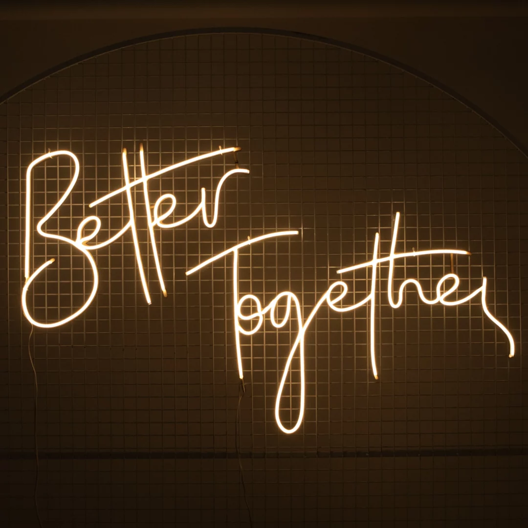 Neon Better Together. Ledonowy napis "Better Together" o ciepłej, białej barwie światła, zapalony, w ciemnym otoczeniu, przyczepiony na kratownicy. Idealna dekoracja tworząca przytulny i nowoczesny klimat. Doskonale sprawdzi się jako element scenografii na ślubach, weselach, eventach walentynkowych i innych romantycznych okazjach. Oferujemy wynajem takich dekoracji na rent4events.pl oraz rent4weddings.pl - rent4events.pl wypożycz wrażenia, rent4wedding.pl zachowaj wspomnienia.