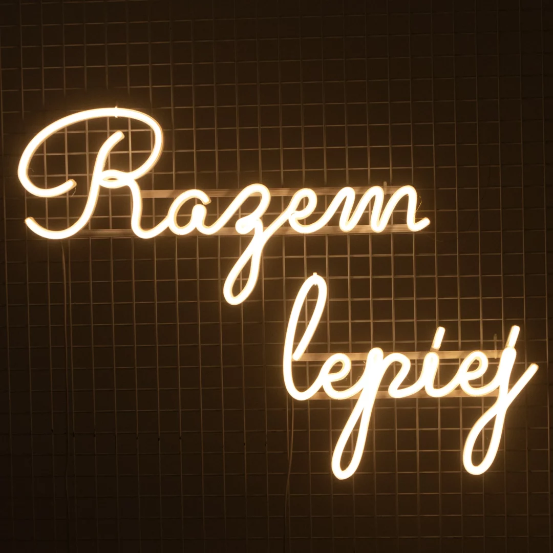 Neon Razem Lepiej. Ledonowy napis "Razem Lepiej" o ciepłej, białej barwie światła, zapalony, w ciemnym otoczeniu, przyczepiony na kratownicy. Idealna dekoracja tworząca przytulny i nowoczesny klimat. Doskonale sprawdzi się jako element scenografii na ślubach, weselach, eventach walentynkowych i innych romantycznych okazjach. Oferujemy wynajem takich dekoracji na rent4events.pl oraz rent4weddings.pl - rent4events.pl wypożycz wrażenia, rent4wedding.pl zachowaj wspomnienia.