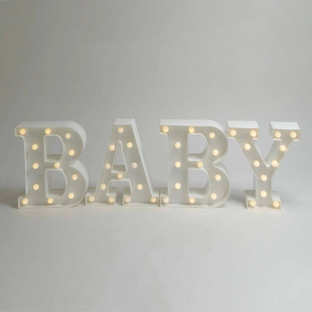 Napis BABY LED, zapalony. Białe litery 3D z napisem "BABY", z zamontowanymi żarówkami emitującymi ciepłe, żółtawe światło. Idealna dekoracja świetlna na baby shower, wesela, oraz inne eventy. Oświetlony napis dostępny w wypożyczalni dekoracji rent4events.pl we Wrocławiu. Litery stanowią doskonałą scenografię na ślubach i imprezach okolicznościowych. Sprawdź ofertę Rent4Weddings na rent4weddings.pl - rent4events.pl wypożycz wrażenia, rent4weddings.pl zachowaj wspomnienia.