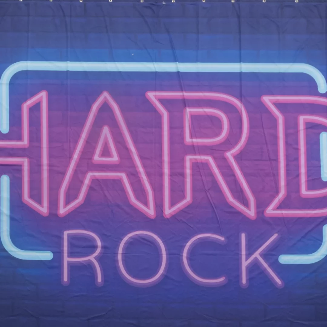 Horyzont Muzyka Hard Rock. Fotograficzne tło przedstawiające neonowy napis "HARD ROCK" w jaskrawo różowym i niebieskim kolorze na ciemnym tle. Tło to doskonale oddaje klimat nocnych imprez i koncertów rockowych, nadając się idealnie na eventy i wesela w klimacie muzyki rockowej. Neonowy styl oraz intensywne kolory w połączeniu z ciemnym tłem tworzą dynamiczny i energetyczny efekt. To tło sprawdzi się na imprezach organizowanych przez wypożyczalnię dekoracji Rent4Events we Wrocławiu - rent4events.pl wypożycz wrażenia, rent4wedding.pl zachowaj wspomnienia.