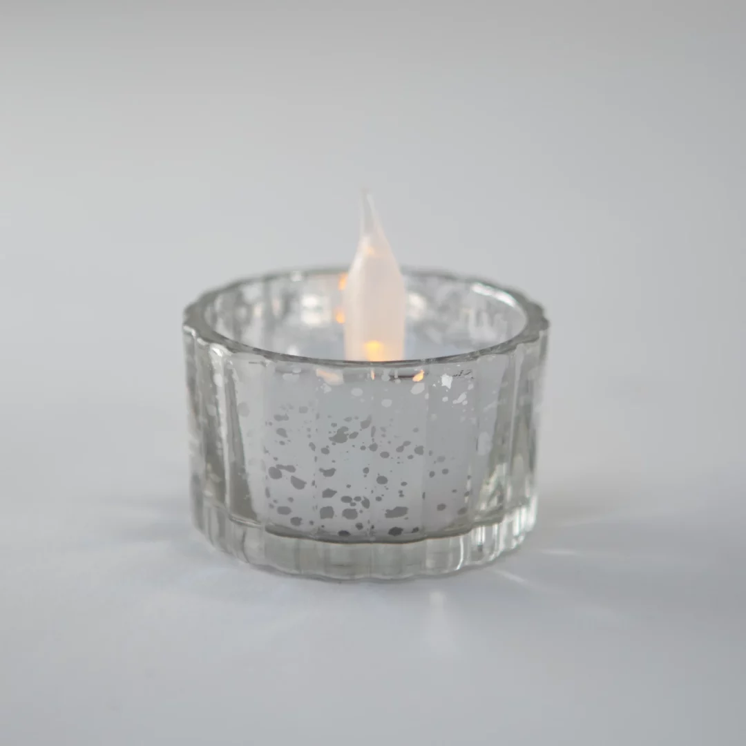 świeczka tealight led umieszczona w eleganckim szklanym świeczniku o srebrzystym, postarzałym wykończeniu, idealna na wesele w stylu glamour i wszelkiego rodzaju eleganckie eventy - od romantycznych kolacji we dwoje, po gale i bankietyl. szklany świecznik z metalicznymi refleksami i delikatnym kropkowanym wzorem dodaje dekoracji vintage elegancji, a ciepłe światło led tworzy przytulny, romantyczny nastrój. ta wyjątkowa kompozycja świetnie sprawdzi się na wydarzeniach we wrocławiu (i nie tylko) - rent4events.pl – wypożycz wrażenia, rent4weddings.pl – zachowaj wspomnienia.